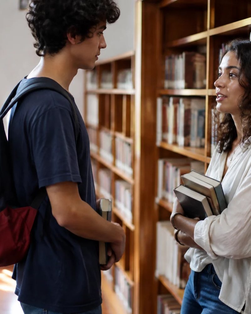 Duas participantes conversando de pé entre as prateleiras de uma biblioteca